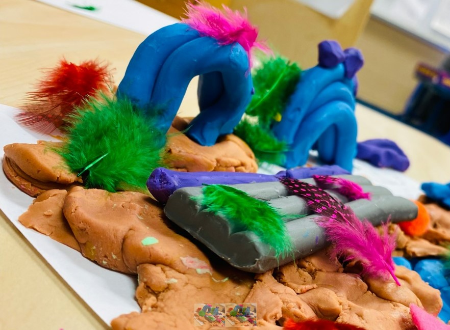 Children's artwork made out of modeling clay and feathers. 
