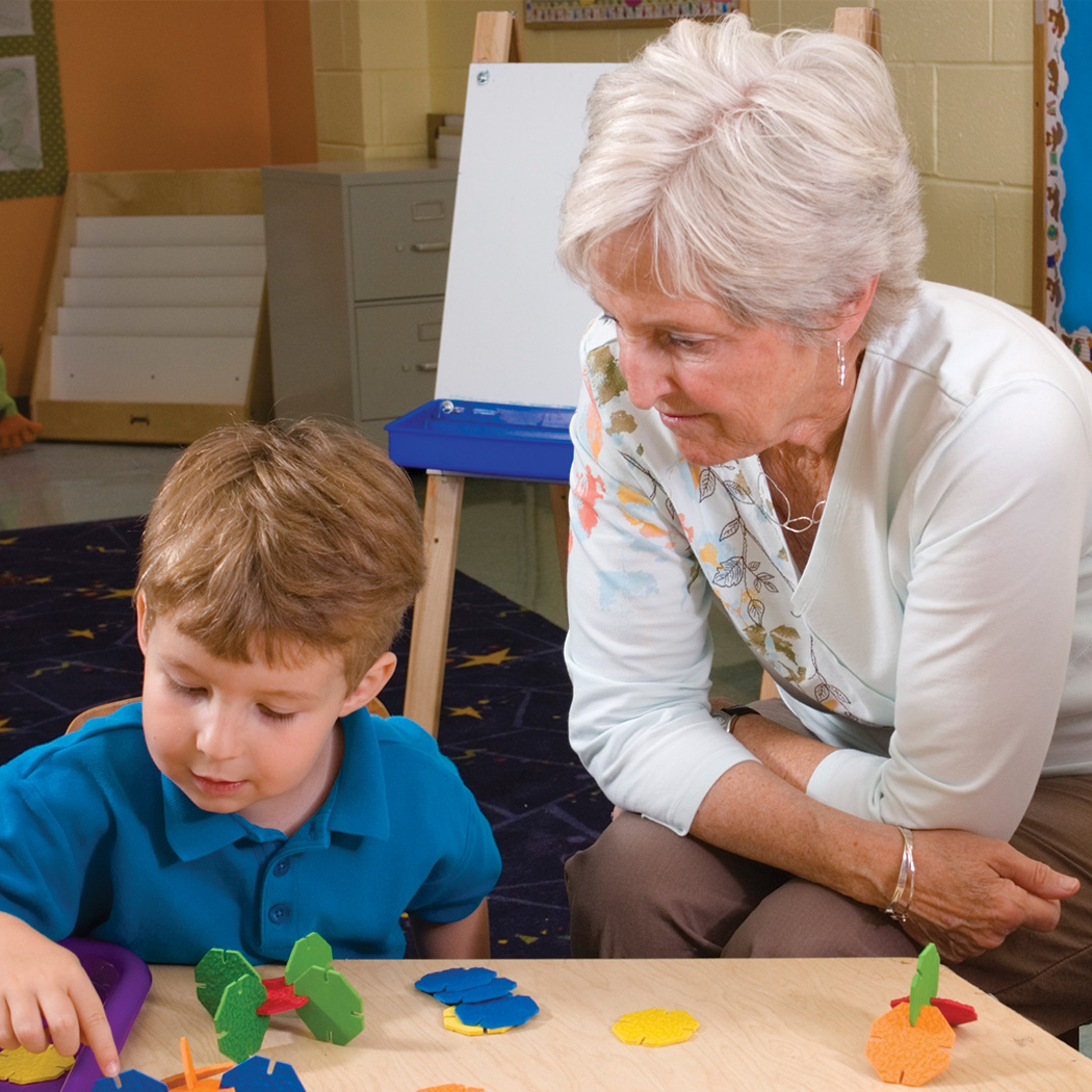 A teacher observes a child working with foam shapes.