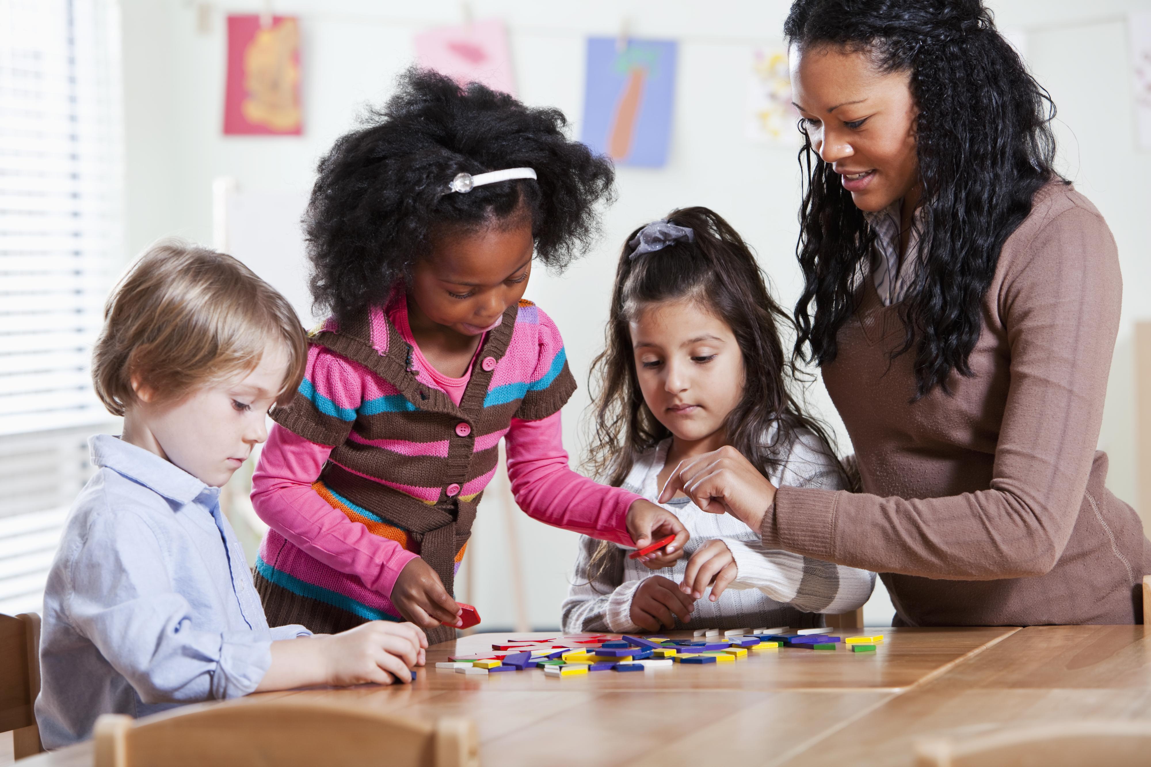 A teacher observes children putting together a puzzle.