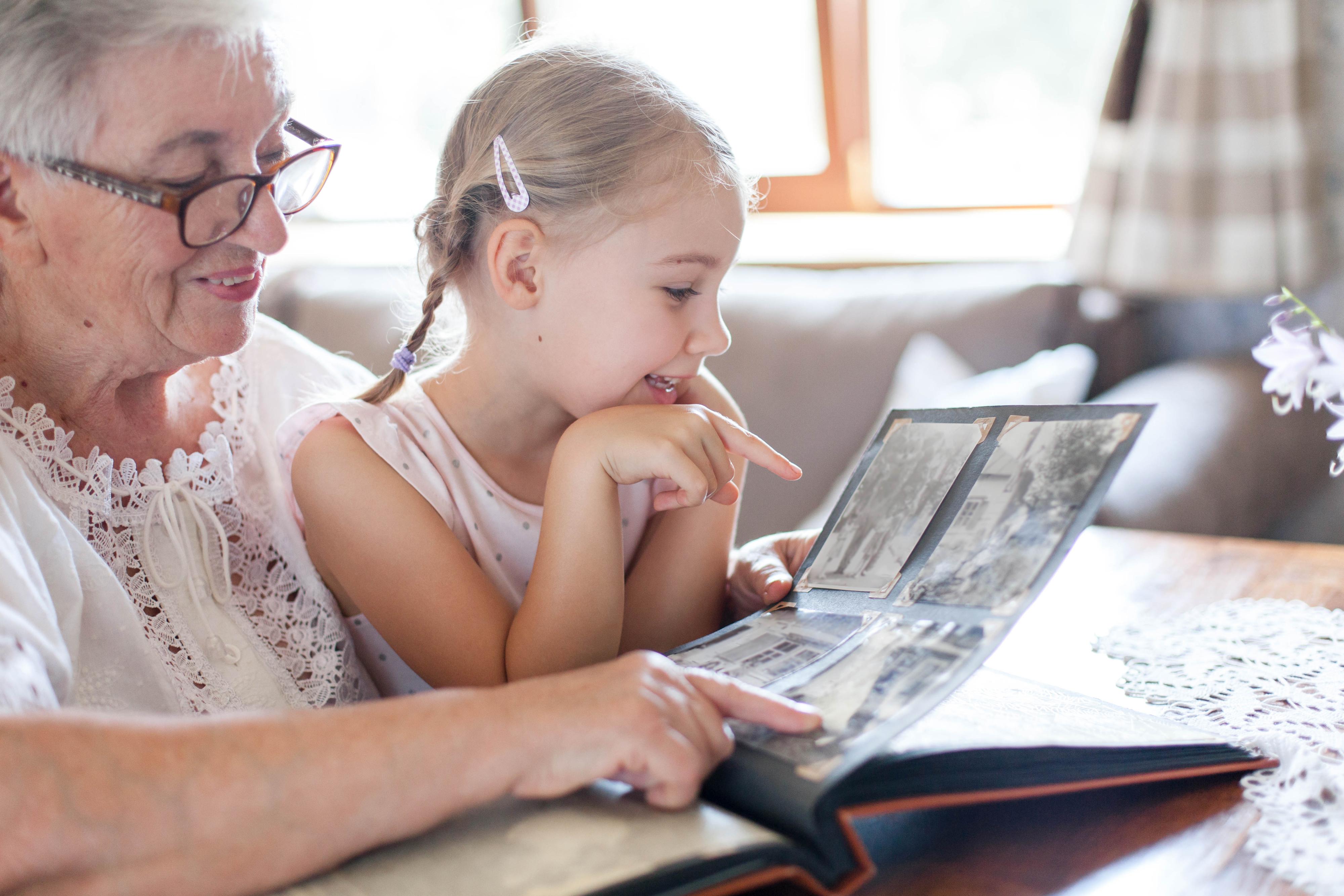 A child and her grandmother look at a scrapbook.