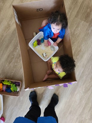 A toddler investigates cornstarch and water while sitting in a box.