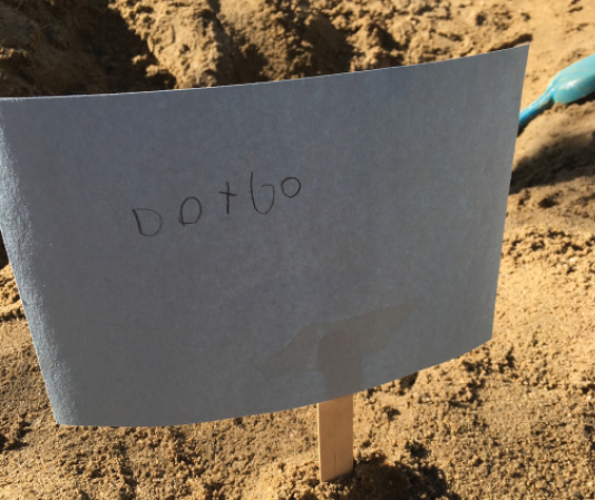 a child's handwritten sign posted in the sand that says "Dont go"
