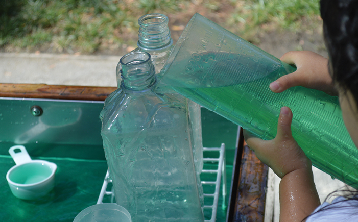 a child pouring water out of a tube into a bottle 