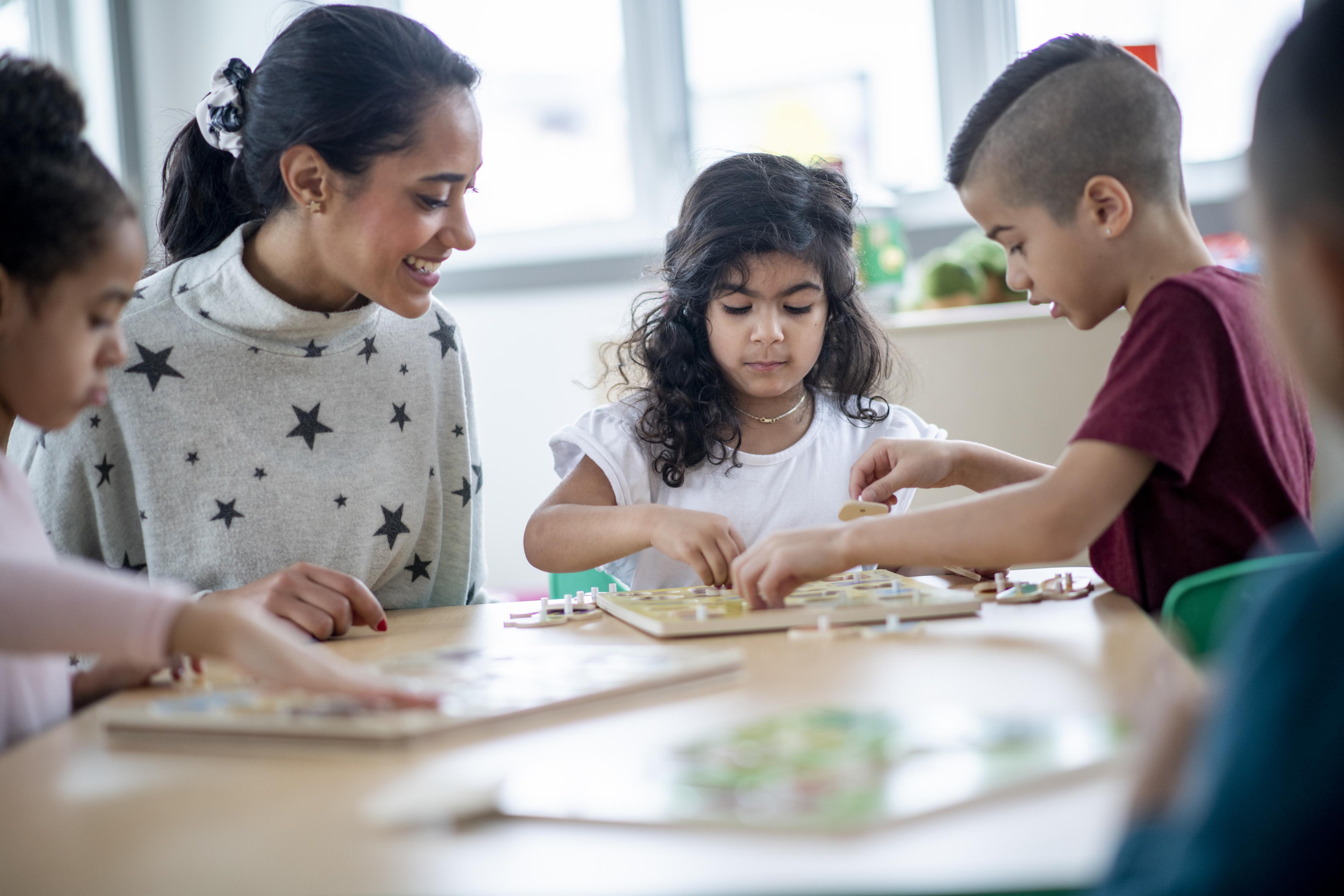 A teacher observes children cooperating with a puzzle.