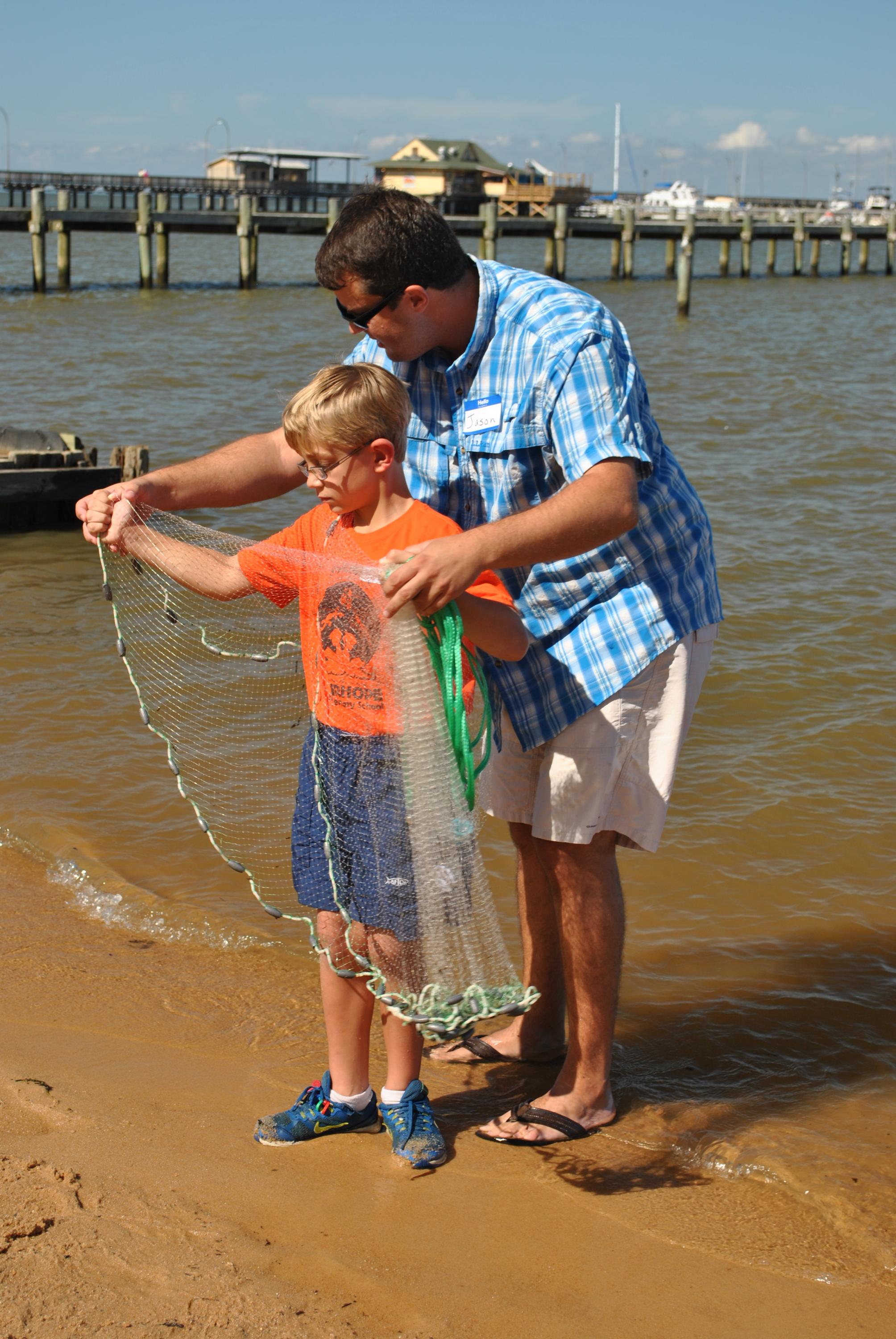 A parent volunteers to teach a child how to throw a cast net.