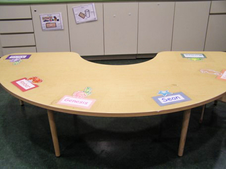 Half-circle shaped table with labels featuring student names taped at intervals on the tabletop