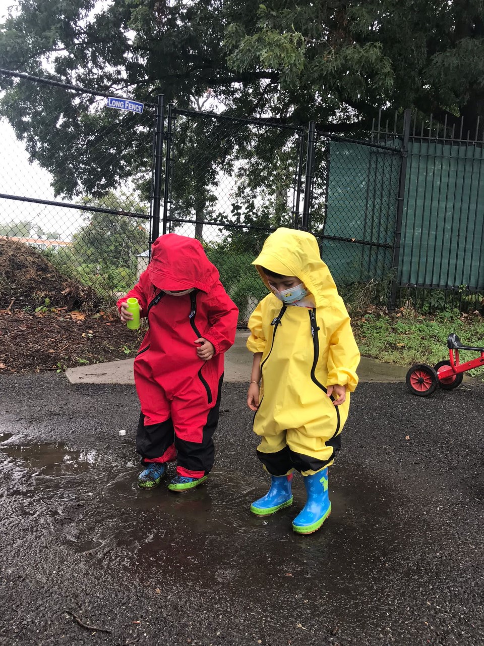 Two children in rain suits explore a puddle