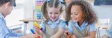 Two preschool girls in a classroom laughing and playing with blocks