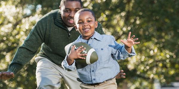 Father and son running and playing with a football outdoors