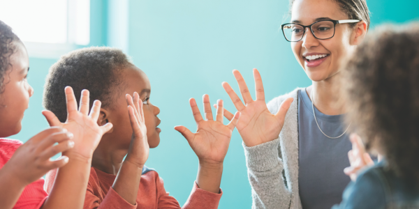 Teacher and three preschool students with hands in air