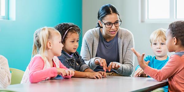 Preschool teacher guides students at table