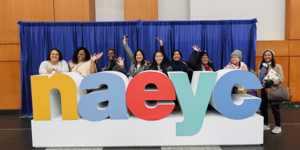 a group of people posing with a large statue of letters spelling n a e y c