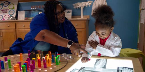 A teacher works with a child at the light table.