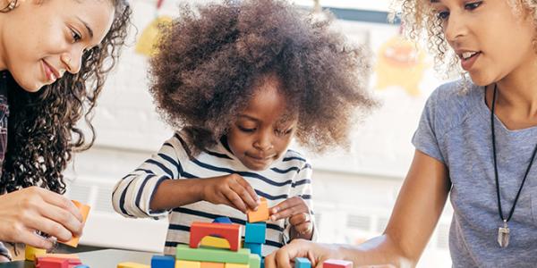 Two women and a young girl sitting at a table and playing with blocks