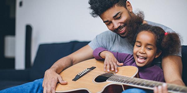 Father and daughter playing guitar on couch