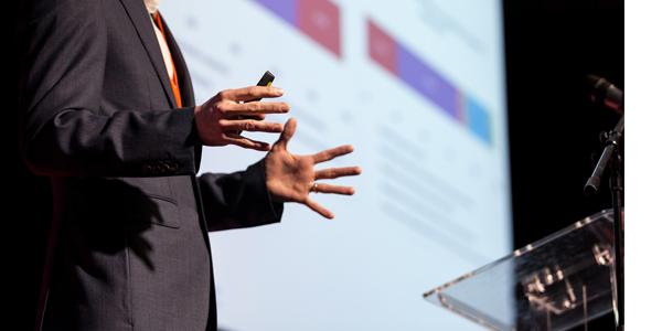 A person speaking on a stage near a podium