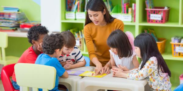 A teacher showing children a picture on a table