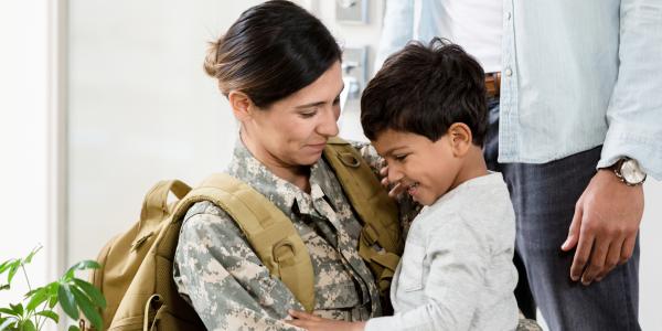 a military mom in camo gear giving her young child a hug