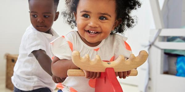 Toddler girl laughing and riding on a pony toy while toddler boy holds on