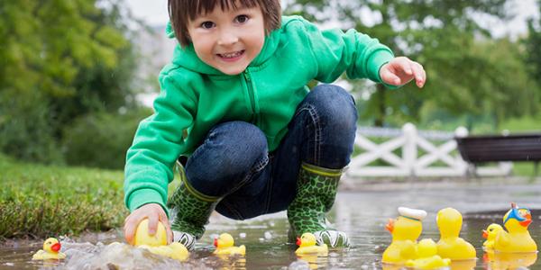Young child playing with rubber duckies in a puddle outside