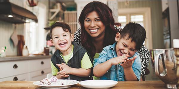 Mother hugging two sons in the kitchen that are sitting in her lap 