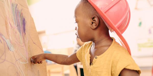 Young boy drawing on a canvas wearing a red hat