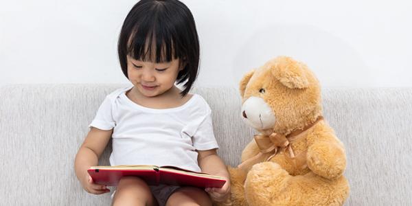 Young girl reading next to a teddy bear