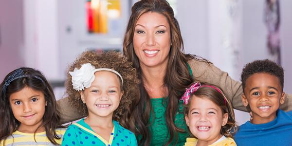 Teacher and preschoolers smiling in a classroom