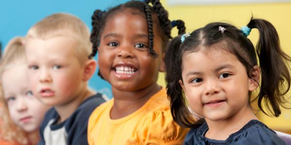 Young children in a line smile for a photograph. 