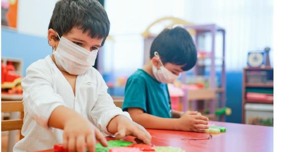 Two children playing in a classroom wearing protective masks.