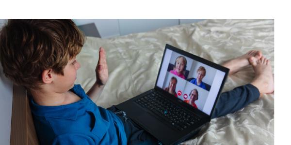 a young boy waving at other children on a video call on the computer 