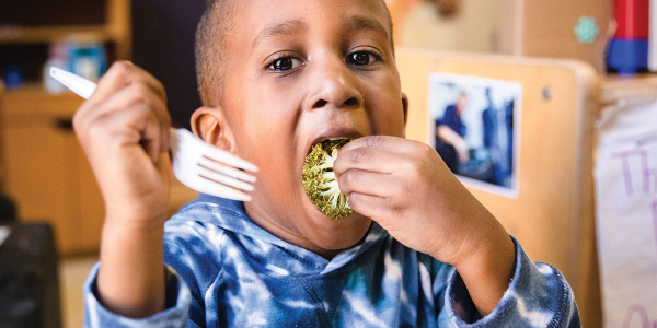 A child eats a piece of broccoli.