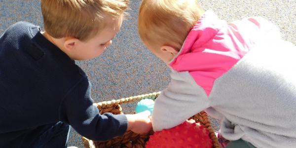 Two children look through a basket of balls.