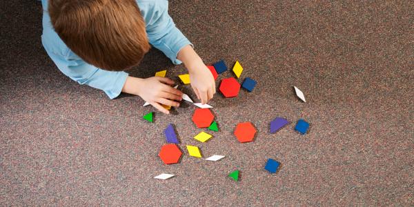 A preschooler plays with geometric shapes on a carpet