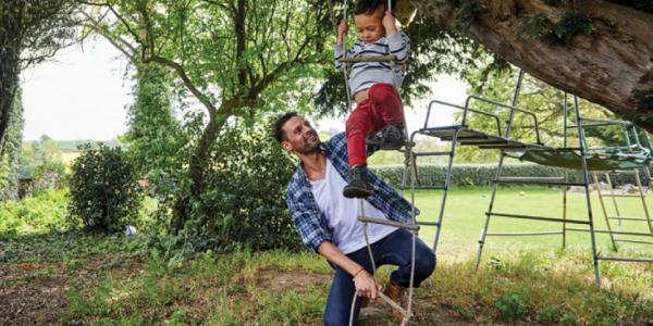 A father plays outside with their child on a rope ladder
