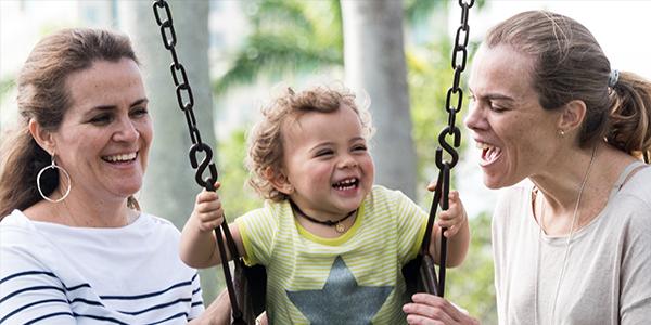 Two adults play with a young child on a swing