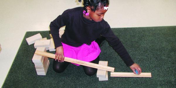 A young girl plays with blocks to make a ramp