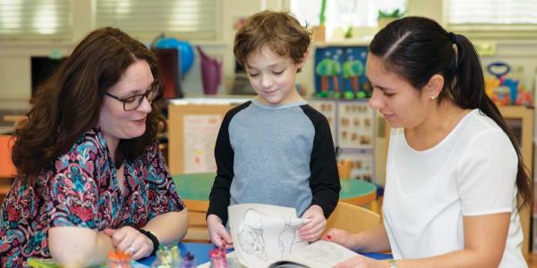 Two teachers looking at book with student