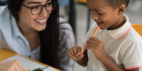 Teacher working with a young child as he writes in a notebook