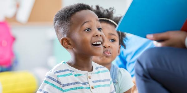 A young boy looking excited and happy as his teacher reads a book.