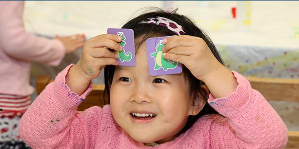 Preschool girl smiling as she holds up two matching cards