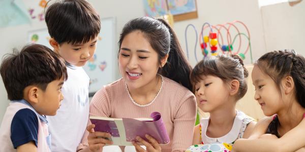 a teacher reading a book surrounded by children