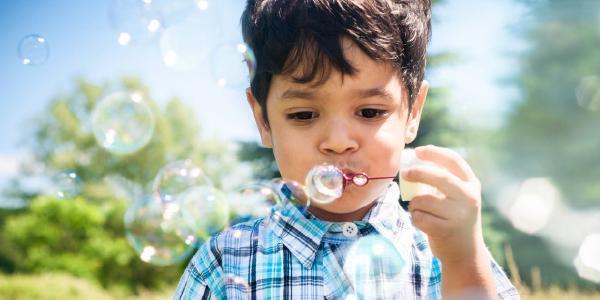Preschool aged boy blowing bubbles outside