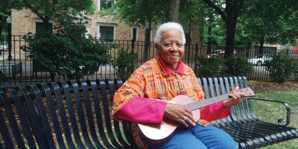 Ella Jenkins sitting on a bench with a guitar in her hands