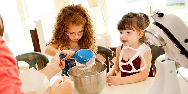 Two young girls baking with a parent