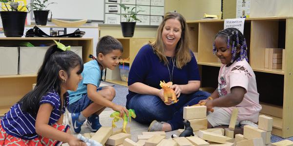 Teacher and students playing with dinosaurs and blocks in the classroom