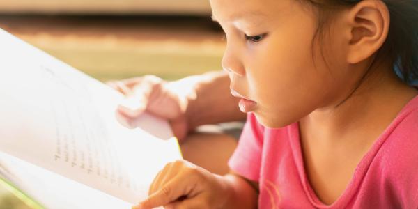 Child focusing intently on book and running her finger along a line of text