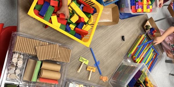 Table full of tinkering materials like blocks, straws, counting cubes, clothespins, and more