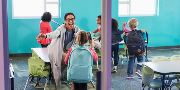 A teacher welcoming her students into the classroom.