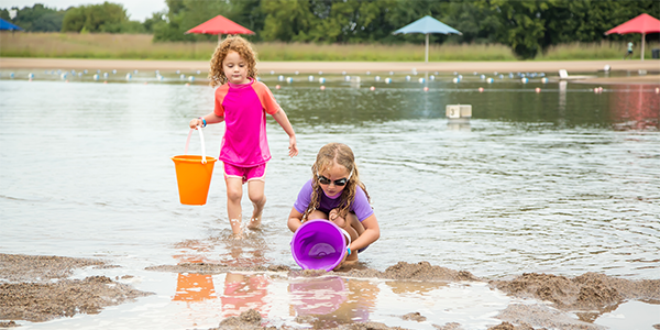 Two young girls at the lake scooping water into buckets